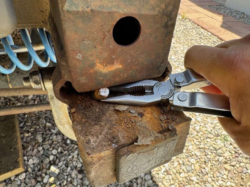 Using pliers to try to extract the broken bolt from the frame rail, as it is still attached to the nut-plate.