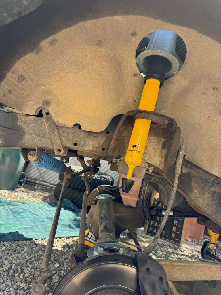 Feeding the shock tower assembly through the fender access hole to position it atop the spring seat in the Land Rover Defender 110