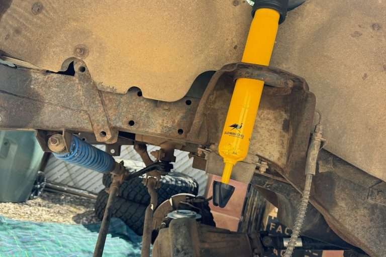 Feeding the shock tower assembly through the fender access hole to position it atop the spring seat in the Land Rover Defender 110