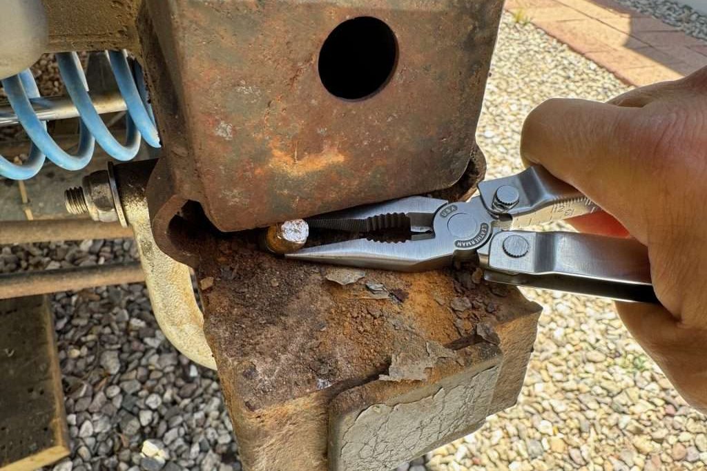 Using pliers to try to extract the broken bolt from the frame rail, as it is still attached to the nut-plate.